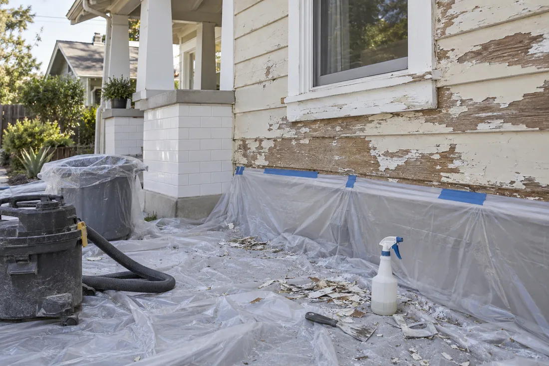 Lead-safe exterior painting setup with plastic sheeting on the ground below a Craftsman wall