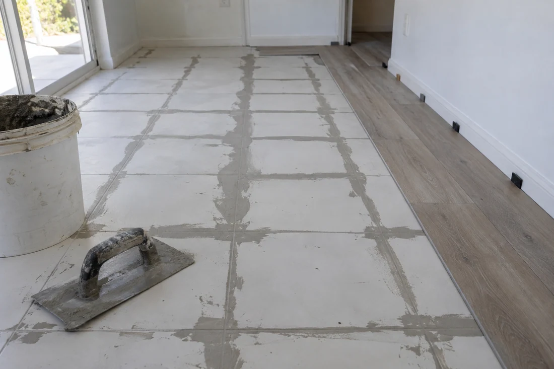Old white tile floor with grout lines skim-coated flat before vinyl plank goes over it