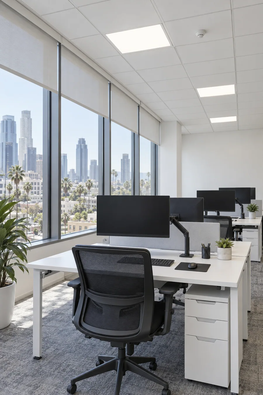 Flat LED panels in a white ceiling grid lighting rows of workstations in a Los Angeles office