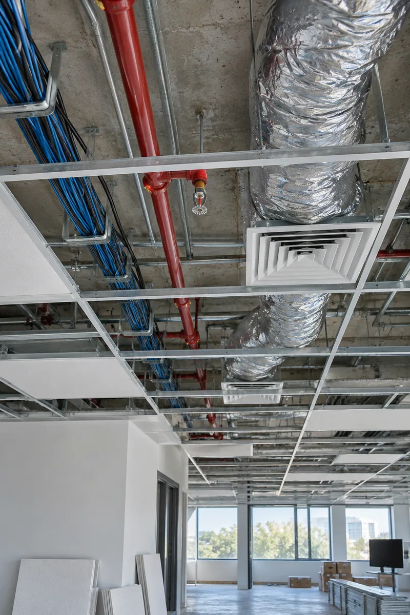 Open ceiling grid in an office build-out showing sprinkler pipe, flexible ducts and new cabling above