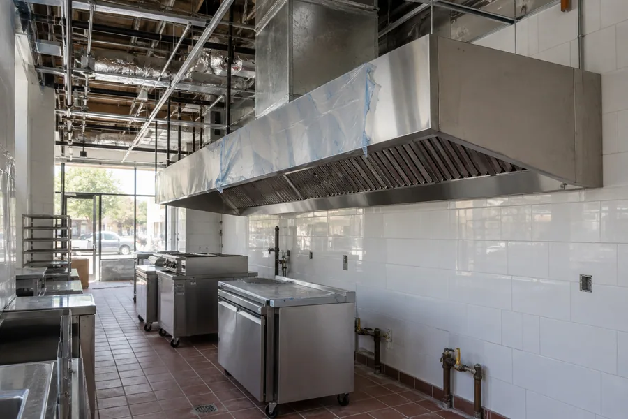 Newly installed commercial hood over an empty restaurant cook line, with the grease duct rising into the ceiling