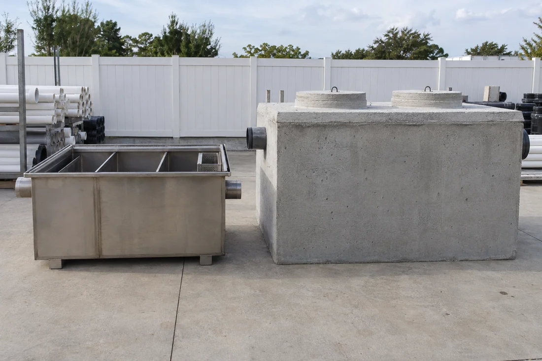 Compact hydromechanical grease interceptor and a large precast gravity interceptor tank side by side at a supply yard