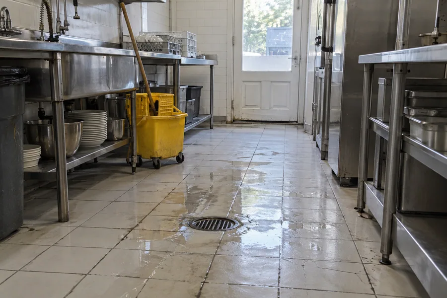 Puddle standing on an old restaurant kitchen floor beside a drain that sits too high