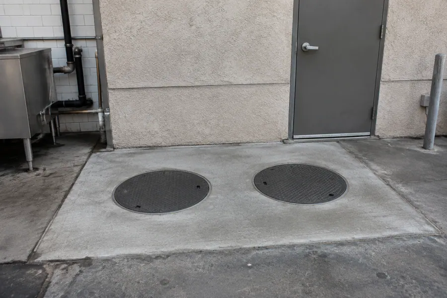 New in-ground grease interceptor with round access covers set in a concrete slab behind a Los Angeles restaurant